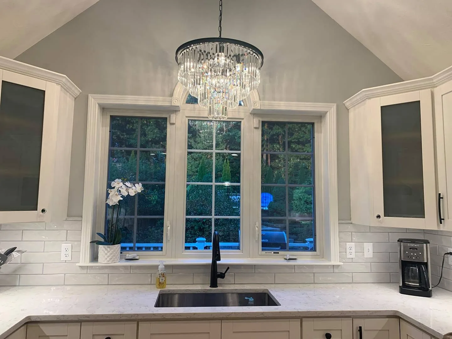 White stone countertop below a chandelier-lit kitchen window