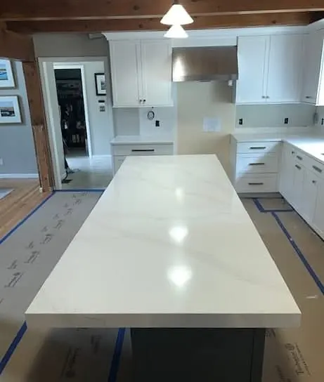 Long white stone island in a completed kitchen.
