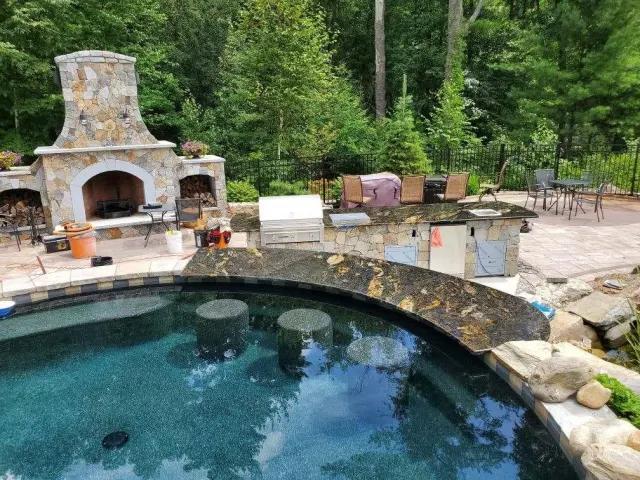 Stone pool hardscape and outdoor fireplace in a completed landscape.